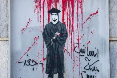 A student in graduation clothes. The writing says humanity is better than war. Photo.